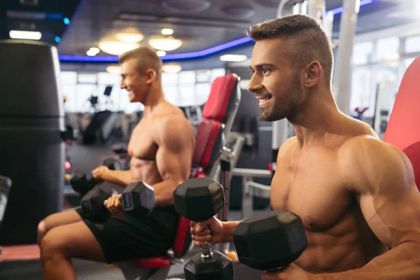 Hombres musculosos jóvenes haciendo ejercicio con pesas en el gimnasio — Foto de Stock
