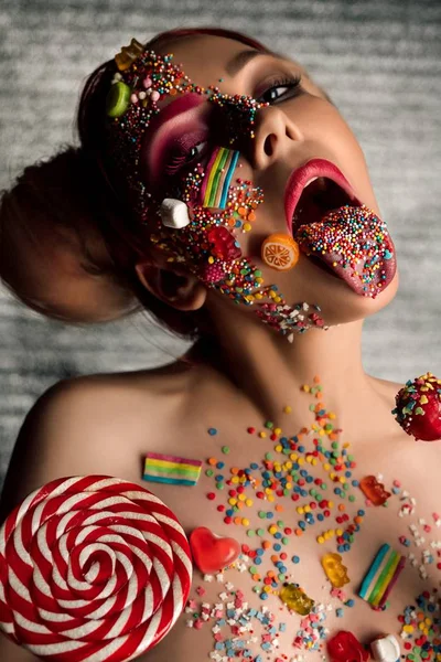 Chica delgada con caramelo en la cara, el cuerpo y la lengua —  Fotos de Stock