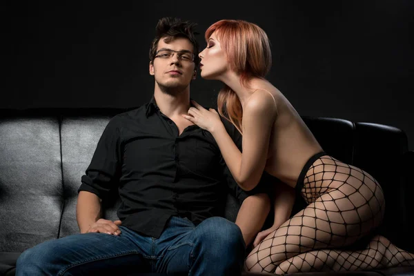 Sexy jovem casal em um sofá de couro preto tiro — Fotografia de Stock