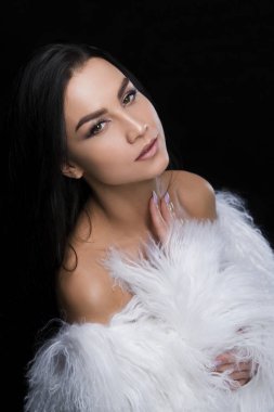 Esmer, beyaz kürk manto giymiş.