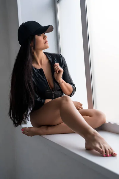 Sexy Brünette mit schwarzer Baseballkappe auf der Fensterbank — Stockfoto