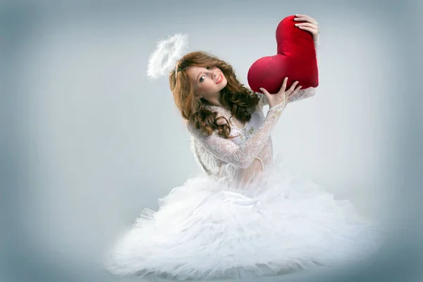 Menina vestida de anjo posando com o coração de pelúcia — Fotografia de Stock