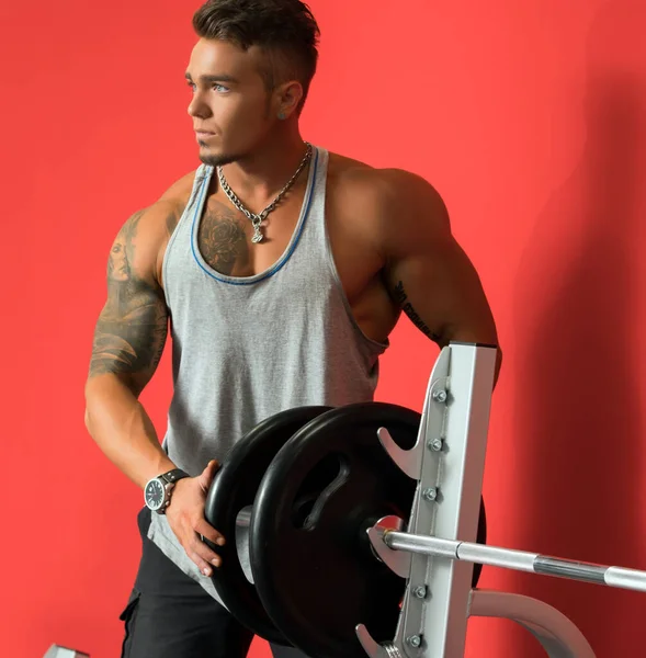 Tattooed young athlete standing near barbell — Stock Photo, Image