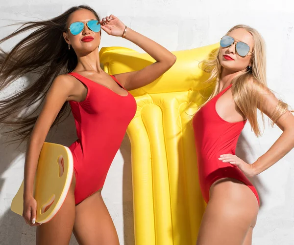 Две сексуальные девушки с жёлтым надувным матрасом возле солнечной стены — стоковое фото
