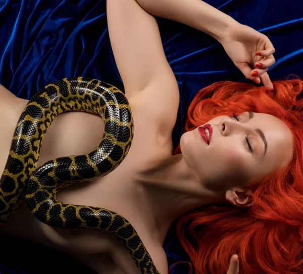 Menina nua de cabelos vermelhos na cama com python tiro — Fotografia de Stock