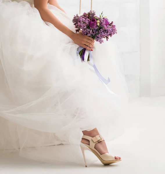 Beautiful bride with bouquet on a swing in studio — Stock Photo, Image