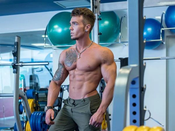 Muskulöser junger Mann posiert im Fitnessraum — Stockfoto