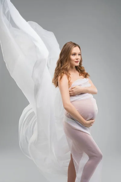 Těhotná žena střílel proti šedé pozadí — Stock fotografie