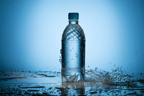 Água limpa salpicando perto de garrafa de plástico translúcido — Fotografia de Stock