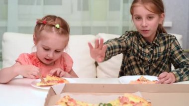 küçük kız pizza yiyip elini sallayarak ablası