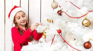 Kırmızı Noel Baba şapkalı küçük kız yeni yıl ağacını süslüyor.