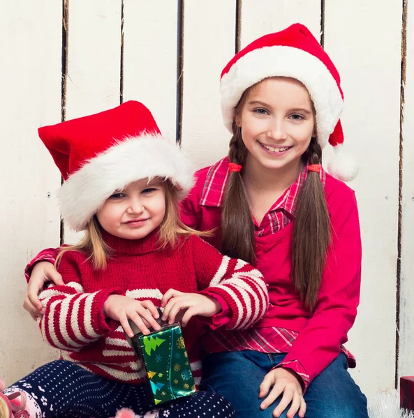 Zwei kleine Mädchen mit roten Hüten sitzen mit Geschenken auf dem Boden — Stockfoto