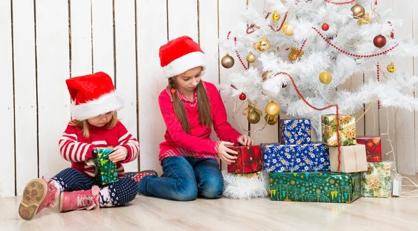 Дві маленькі дівчата відкривають різдвяні подарунки, сидячи на підлозі — стокове фото