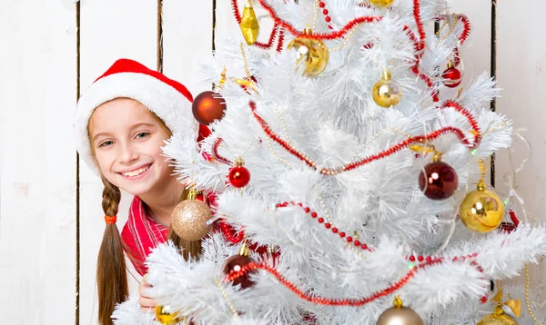 Sorrindo menina espreitando atrás de uma árvore de ano novo — Fotografia de Stock