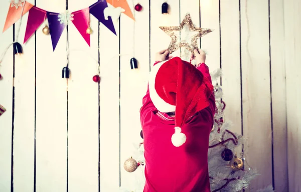 Petite fille en chapeau rouge mettant une étoile sur le dessus de l'arbre de Noël — Photo