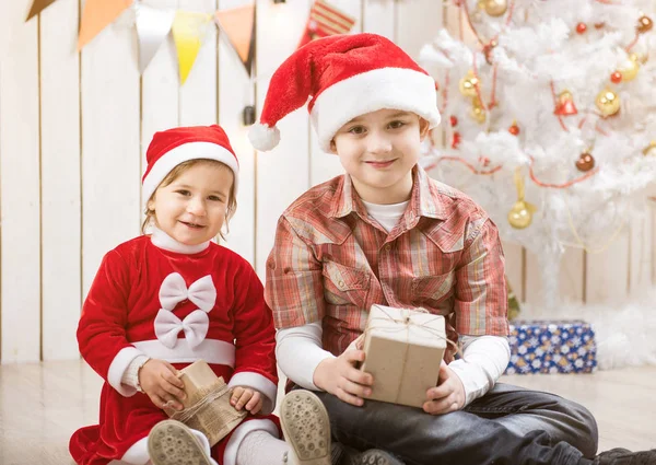 Børn i røde julemandshatte sidder i dekoreret værelse - Stock-foto