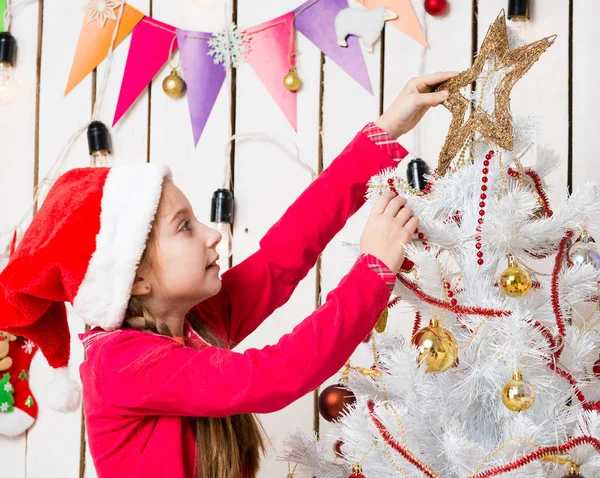 Klein meisje met rode hoed zetten een ster op de top van kerstboom — Stockfoto