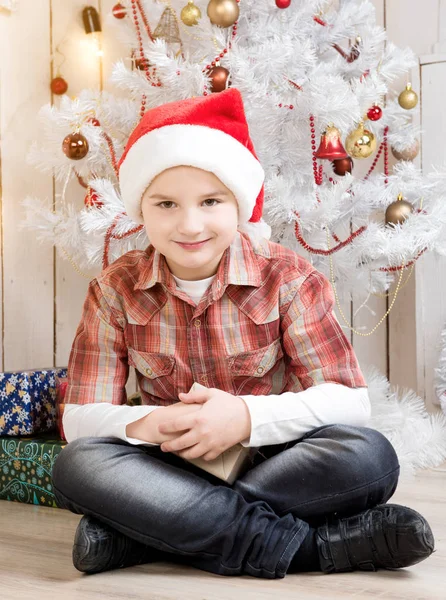 Lilla pojken i röd hatt tar nuvarande box nära nyår träd — Stockfoto