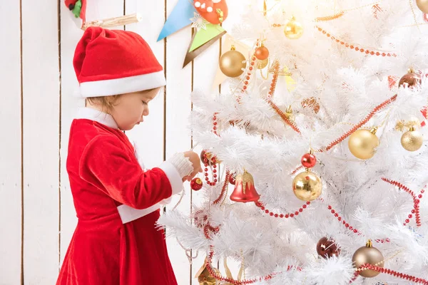 Маленькая девочка в красном костюме украшает новогоднюю елку мячом — стоковое фото