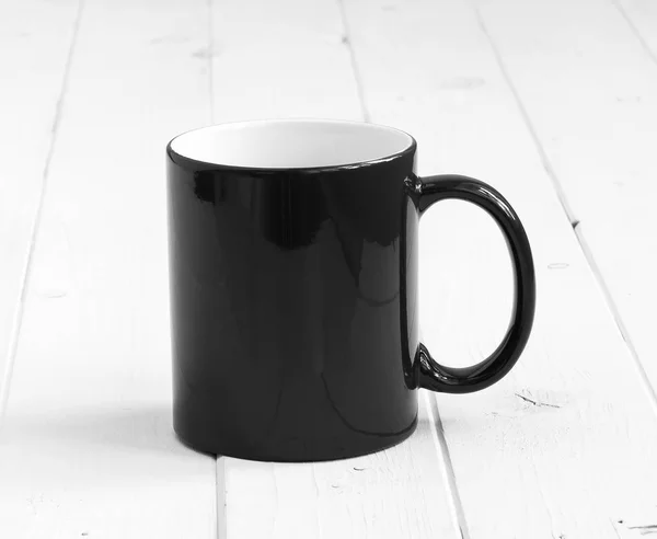 Black cup with white inside on wooden table — Stock Photo, Image