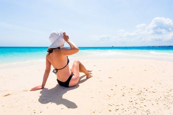 Dziewczyna w kapeluszu siedzi na pięknej plaży — Zdjęcie stockowe