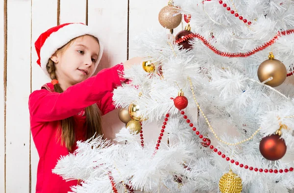 Liten flicka i röd tomte hatt dekorera nytt år träd — Stockfoto