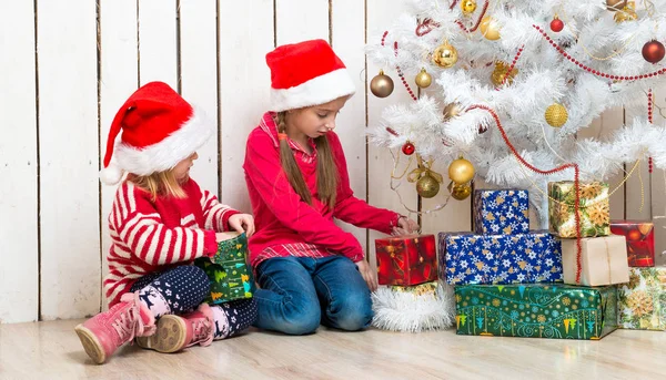 Twee kleine meisjes open kerstcadeaus zittend op de vloer — Stockfoto