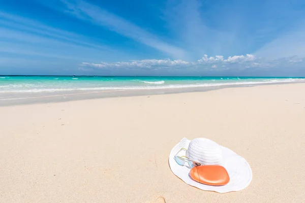 Sombrero blanco, gafas de sol y crema bronceadora en la orilla del mar — Foto de Stock