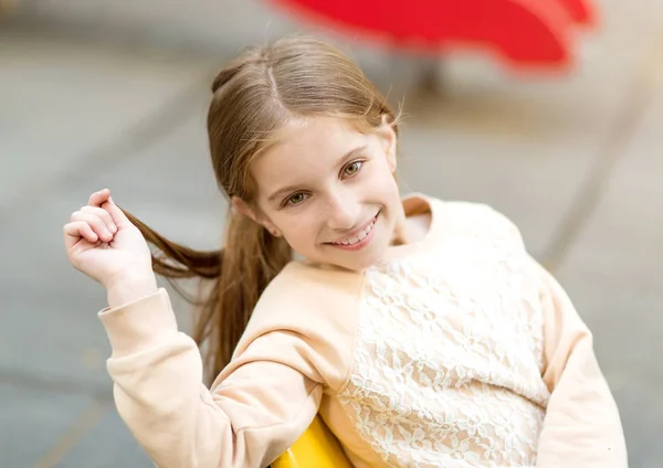 Schattig klein meisje zittend op een stoel met haar in haar hand — Stockfoto