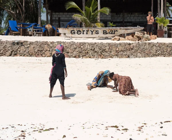Meninas locais que procuram algo na praia de areia perto de bar em Zanzibar — Fotografia de Stock