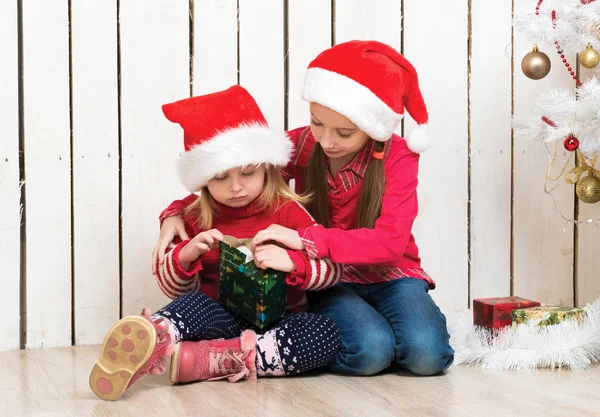 Dwie małe dziewczynki w czerwonych kapeluszach siedzące na podłodze z prezentami — Zdjęcie stockowe