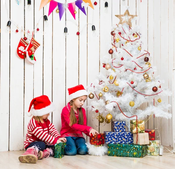 Zwei kleine Mädchen öffnen Weihnachtsgeschenke auf dem Boden sitzend — Stockfoto