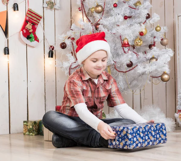 Kleiner Junge mit rotem Hut nimmt Geschenkbox in der Nähe des Neujahrsbaums entgegen — Stockfoto