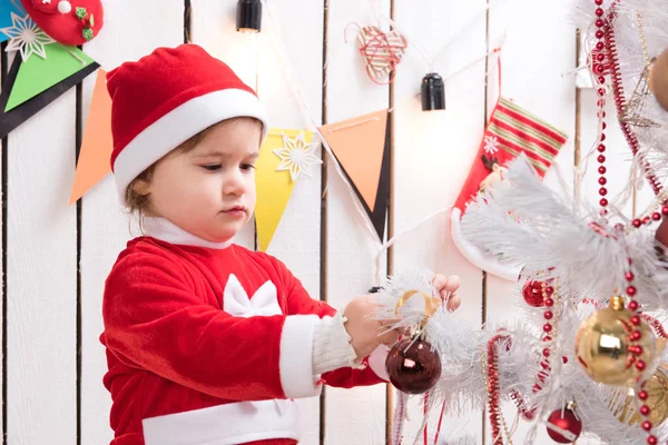 Bambina in costume rosso decora l'albero di Capodanno con la palla — Foto Stock