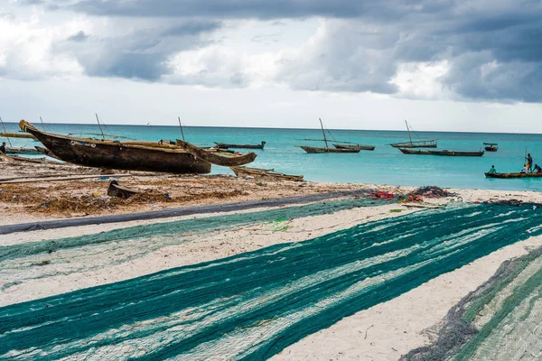 Velké rybářské sítě leží na africké pláži s loděmi poblíž pobřeží — Stock fotografie