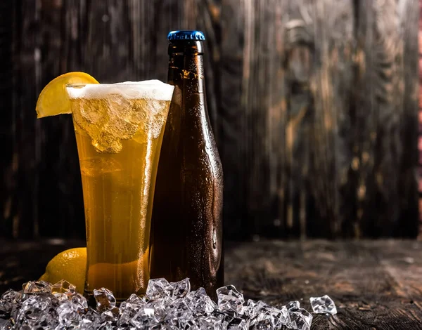 Garrafa e um copo de cerveja com gelo e limão — Fotografia de Stock