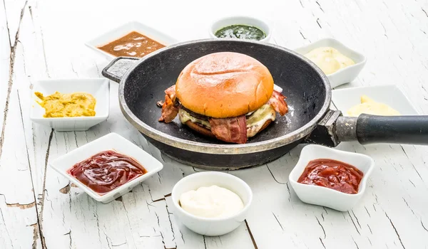 Hamburguesa en una sartén con salsas sobre fondo blanco —  Fotos de Stock