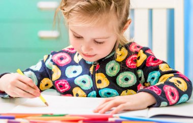 Küçük sarışın kız kalemle resim çiziyor.