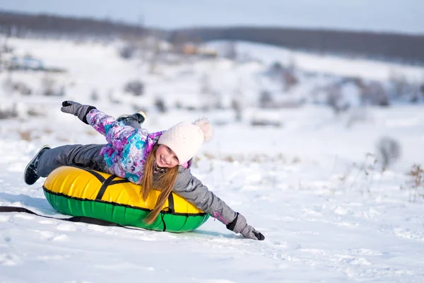 Little girl enjoying snow tubing at sunny weather