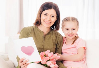 Anne ve kızı kanepede hediyelerle gülümsüyor.