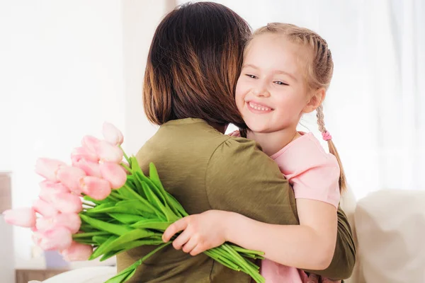 Kind umarmt Mutter, hält Blumen — Stockfoto