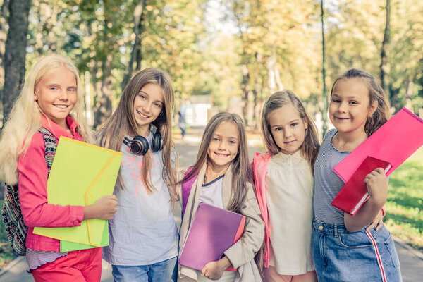 Pretty smiling little girls stand together in the sunshine park