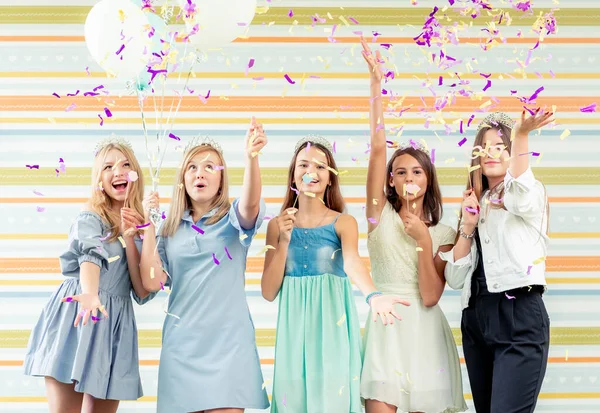 Красивые улыбающиеся девочки-подростки в платьях радостно подняли руки вместе и бегают за шлюхами с блеском на дне рождения — стоковое фото
