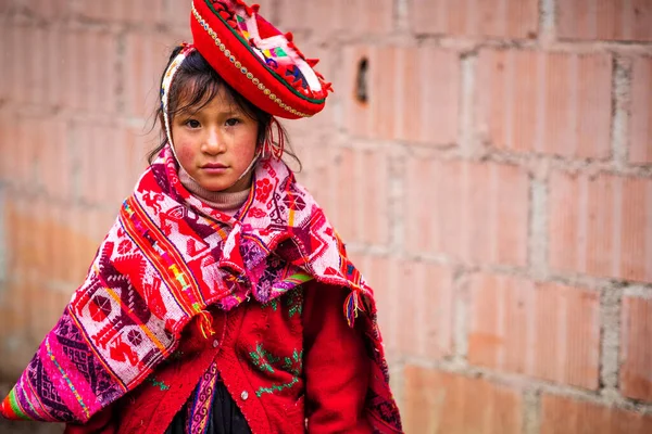 Klein meisje in de nationale rode kleding en hoed op de achtergrond van de muur in Cusco — Stockfoto