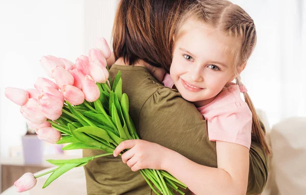 Criança abraçando a mãe, segurando flores — Fotografia de Stock