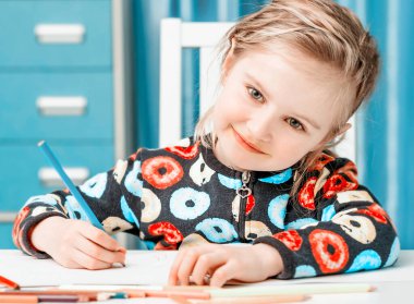 Çekici sarışın küçük kız kalemlerle çiziyor.