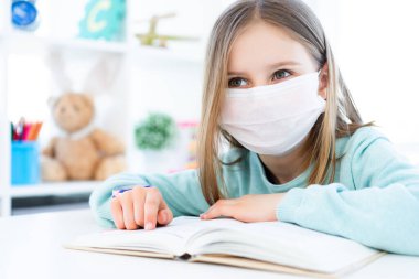 Maskeli küçük kız kitap okuyor.