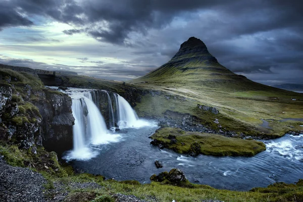 多云 Kirkjufellsfoss Waterfall 与基尔丘山山在冰岛背景中的阴暗的一天。长时间曝光. 图库图片