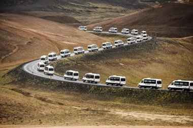 Tur otobüs minibüs İzlanda'daki bir dağ manzarası ile önde gelen bir eğri yolda.