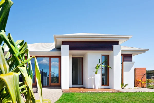 Moderne Villa mit Rasen in der Nähe eines langen Laubbäumchens und blauem Himmel — Stockfoto